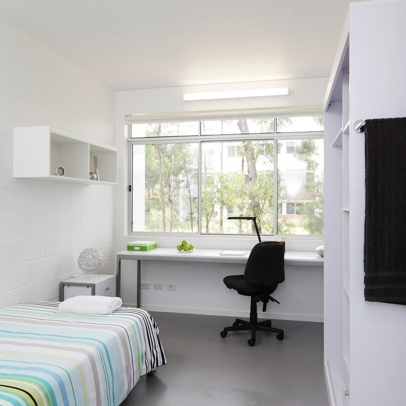 Griffith University Village のシェアアパートの個室。キングシングルベッド、窓に面した学習デスク、備え付けの棚とワードローブ